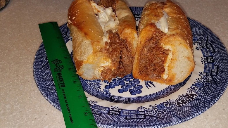 Two sandwich halves on a blue plate with a green ruler.