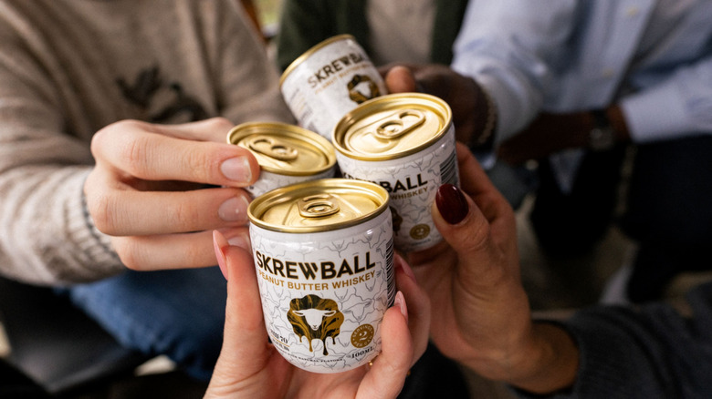 Group of people holding up their Skrewball Whiskey cans to cheers.