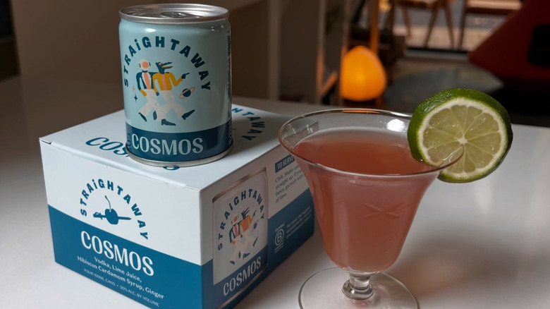 A Straightaway Cosmos can resting on its product box next to a prepared Cosmos in a glass.