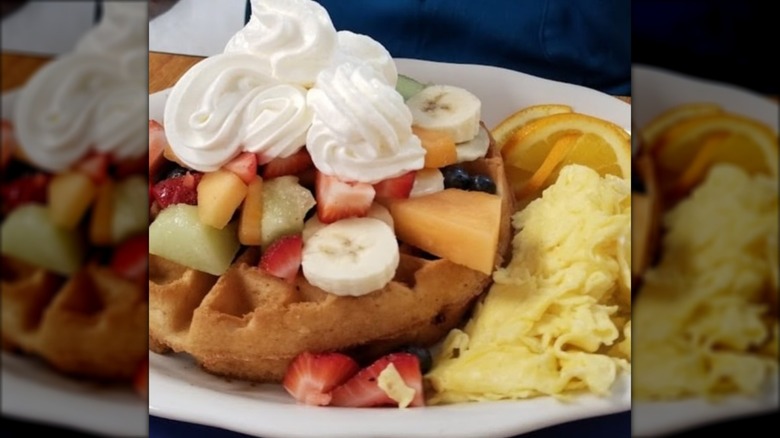 Waffle covered with fruit, whipped cream, and eggs on the side.