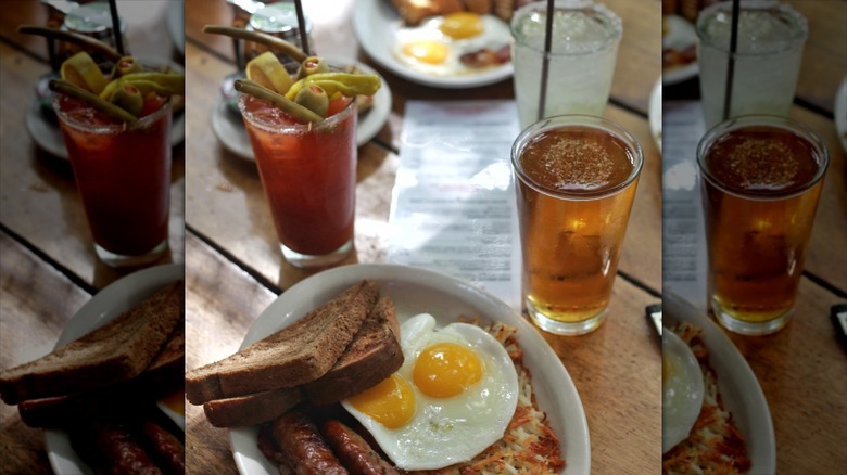 Diner table with plates of eggs, sausage, and toast with cocktails.