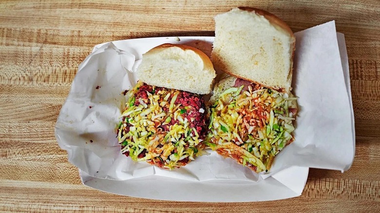 Two open sandwiches with hot sauce, coleslaw, and pork.