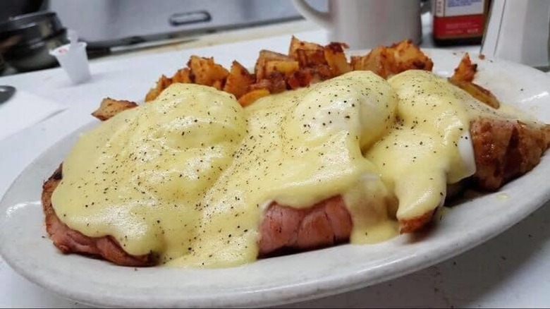 Eggs Benedict on plate with home fries.