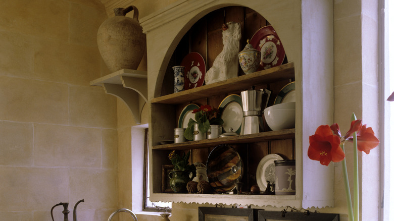 Arch shaped wall mounted shelf displaying plates, sculptures, and other decor inside kitchen