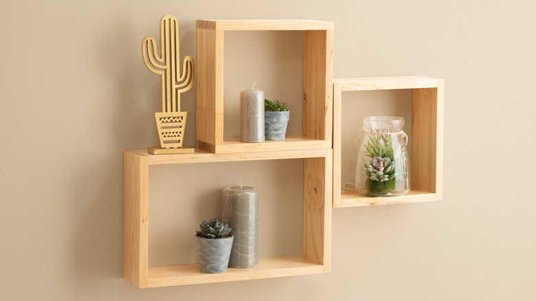 Three wooden wall mounted cubbies holding house plants and silver candles with wood carved cactus decoration