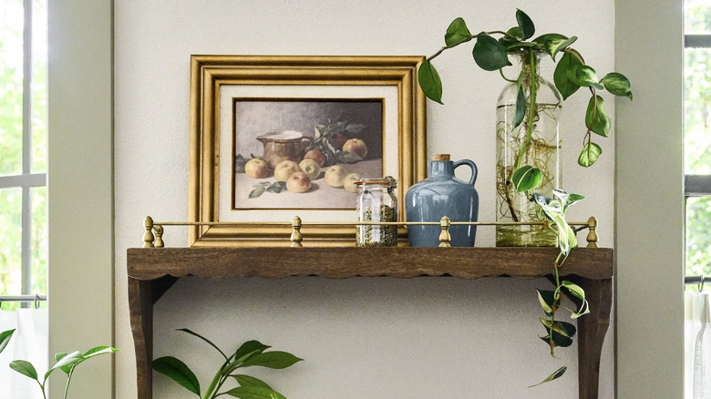 Wooden floating shelf with gold gallery rail holding picture frame, bottles, and plant vase