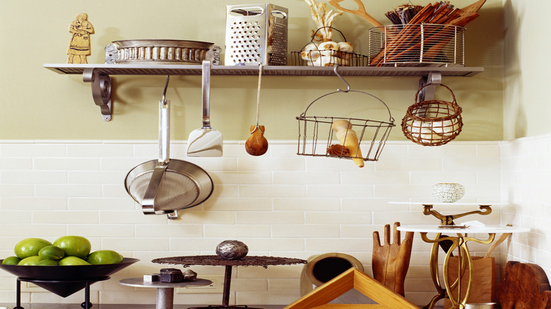 Metal floating shelf on wall holding cooking supplies with utensils and baskets hanging on the edge