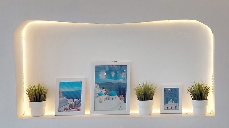 White wall with carved niches holding plants and framed photos