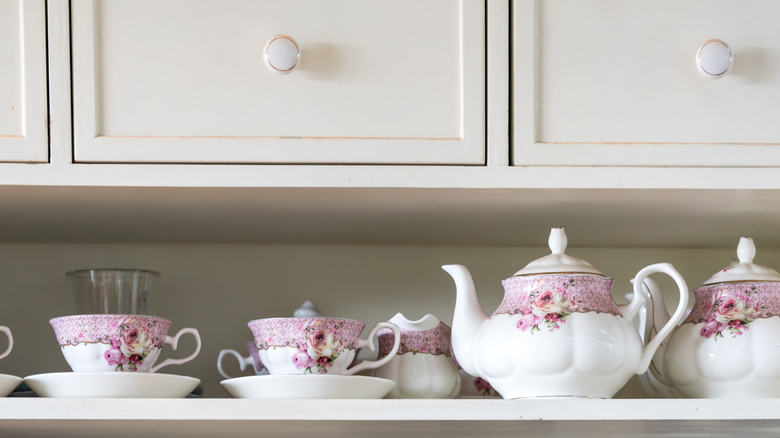 Pink floral designed teacups and teapots on white shelf with drawers above