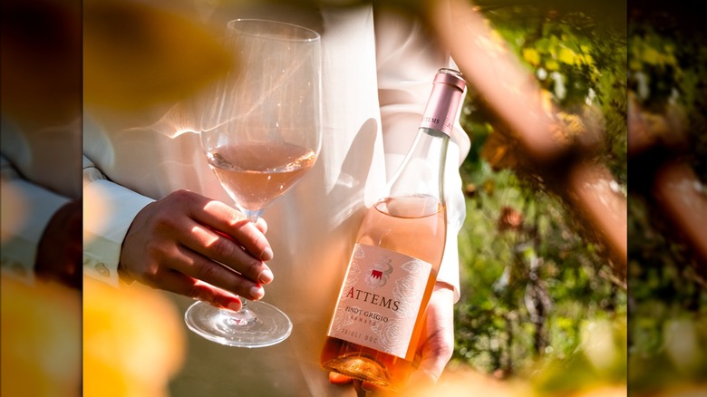 hands holding bottle and glass of orange wine