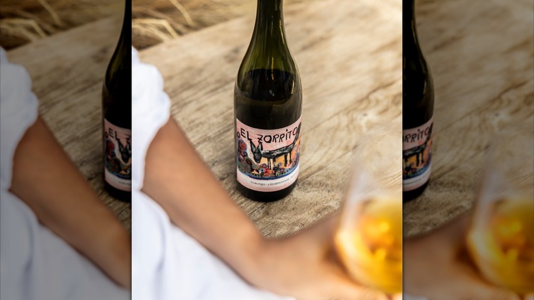 bottle of orange wine with hand holding glass
