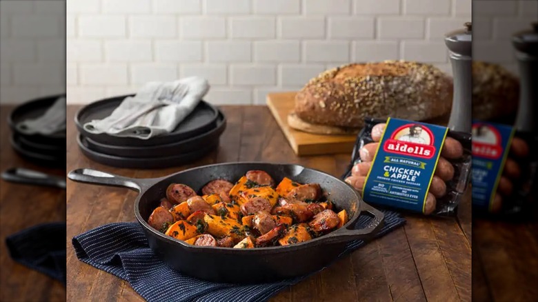 sliced sausage and sweet potatoes cooked in a cast iron skillet with a package of aidells sausage behind