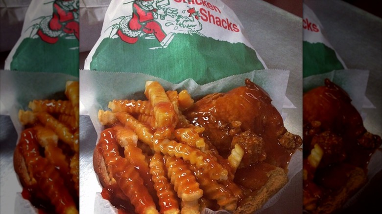 A portion of Harold's chicken with sauce, fries, and a branded red and green bag in the background.
