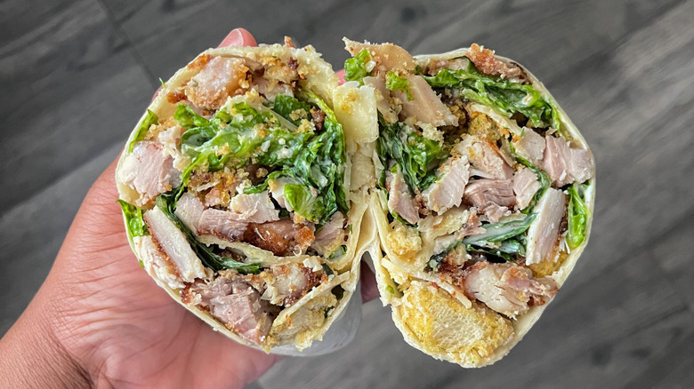 A person holding a chicken Caesar wrap in their hand that's been cut in half showing the lettuce, chicken, and bacon inside