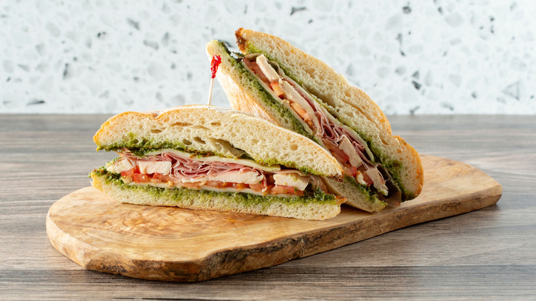 A sandwich sitting on a wooden cutting board with chicken, tomato, and pesto inside