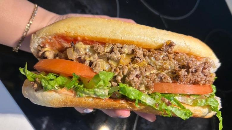 A chopped cheese sandwich on a roll featuring ground beef with melted cheese, onions, lettuce, tomatoes