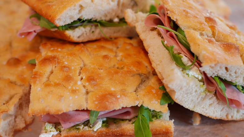 A sandwich filled with greens and deli-sliced meat on Italian focaccia bread