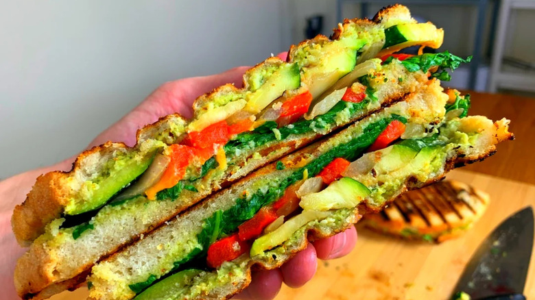 A hand holding a cut panini, showing vegetables inside