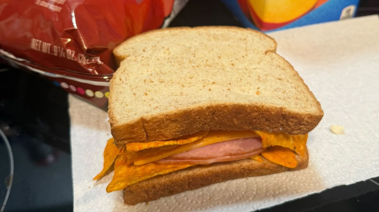 A sandwich filled with ham, cheese, and Doritos on brown bread