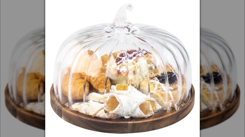 A glass pumpkin dome with a wooden bottom, filled with pastry