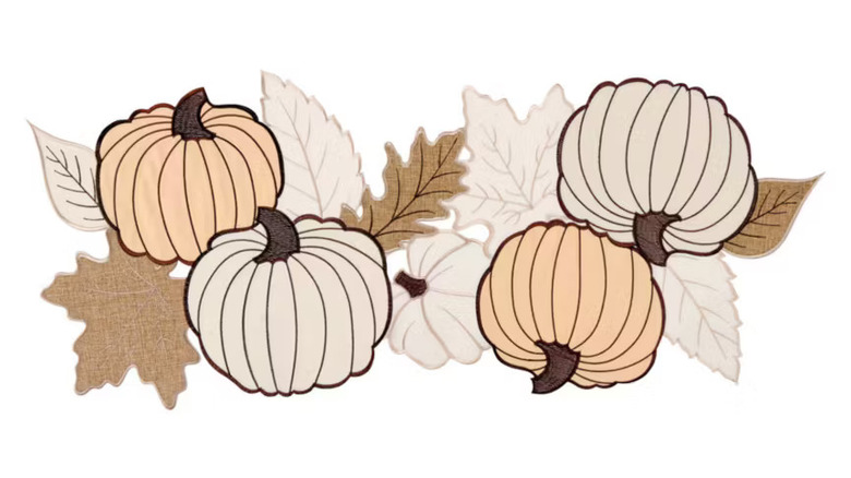 A fabric centerpiece with four pumpkins and fall leaves