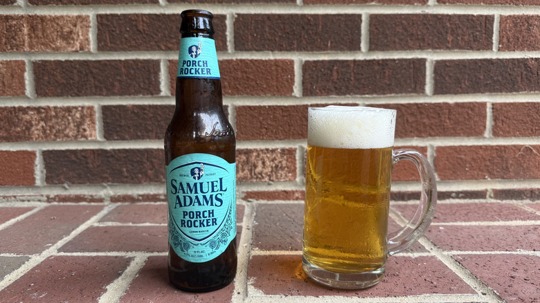 Glass of amber radler next to Samuel Adams bottle on brick surface