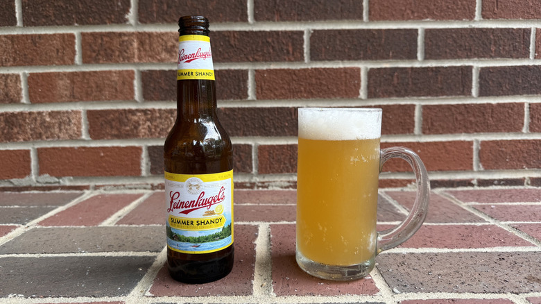 Glass of golden shandy next to Leinenkugel's Summer Shandy bottle on brick surface