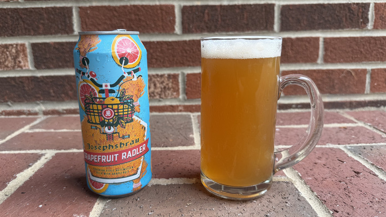 Glass of amber-hued radler next to Josephsbrau grapefruit radler can on brick surface