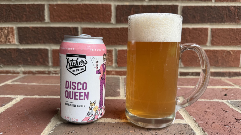 Glass of amber-hued radler next to Two Pitchers Disco Queen can on brick surface