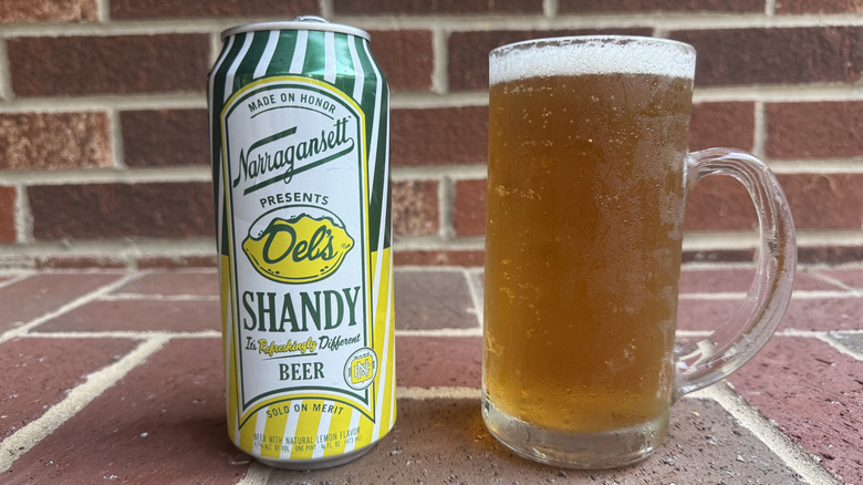 Glass of amber-hued radler next to Del's Shandy can on brick surface