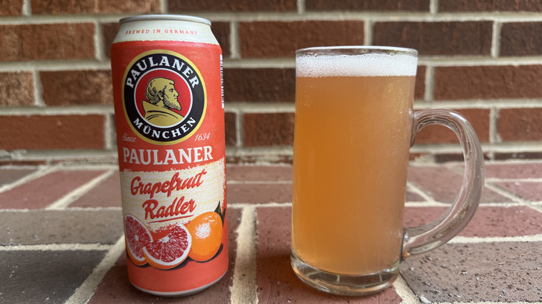 Glass of pinkish orange radler next to Paulaner grapefruit radler can on brick surface
