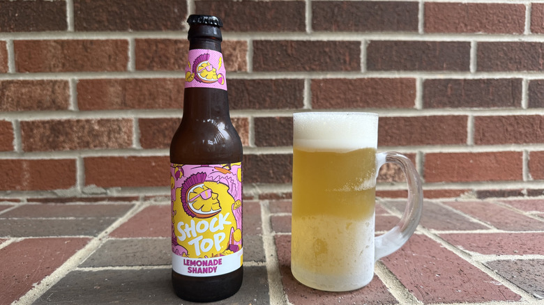 Glass of golden shandy next to Shock Top bottle on brick surface