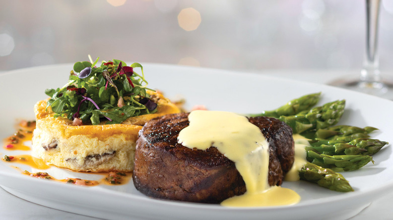 A white plate containing a filet mignon with a mushroom and white cheddar frittata, arugula salad, and asparagus