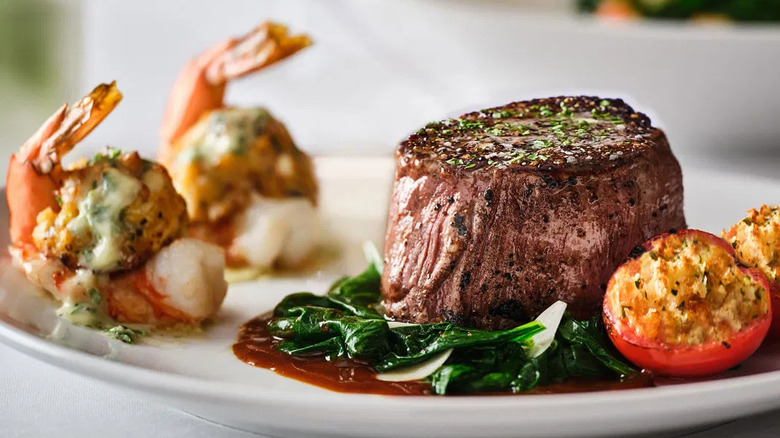 A white plate with an eight-ounce filet mignon and crab-stuffed shrimp with sautéed spinach