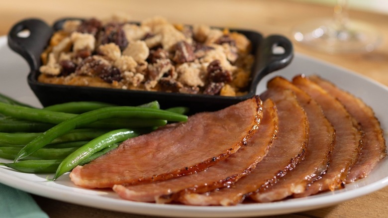 Slices of honey-glazed spiral ham on a white plate with green beans and sweet potato mash