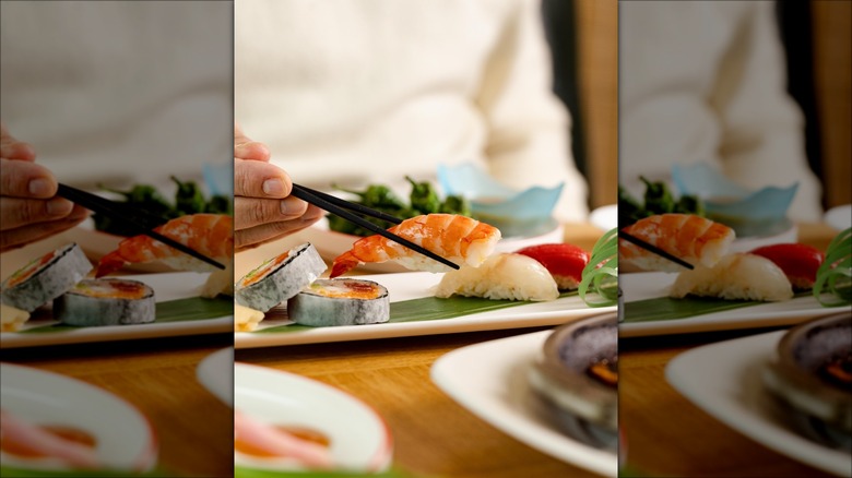 Person holding a piece of sushi with chopsticks over a dish at Nobu London