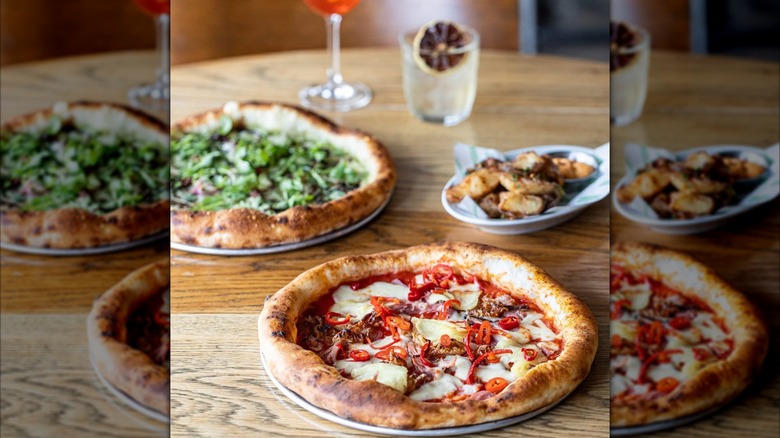 Two Pizza East pizzas with a side dish and drinks on a wooden table