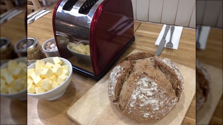 Sourdough loaf next to cubed butter in a bowl, cutlery, and a toaster