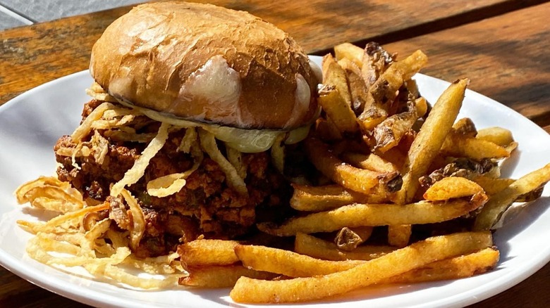 Sloppy joe with onions and jalapeno on plate outside in sun with fries served at Longman & Eagle in Chicago