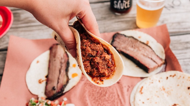 Sloppy Juan taco being held over brisket and tortillas on table at Zavala's Barbecue in Grand Prairie