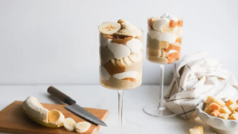 Butterscotch And Miso-Roasted Banana Mini Trifles in wine glasses with banana on cutting board