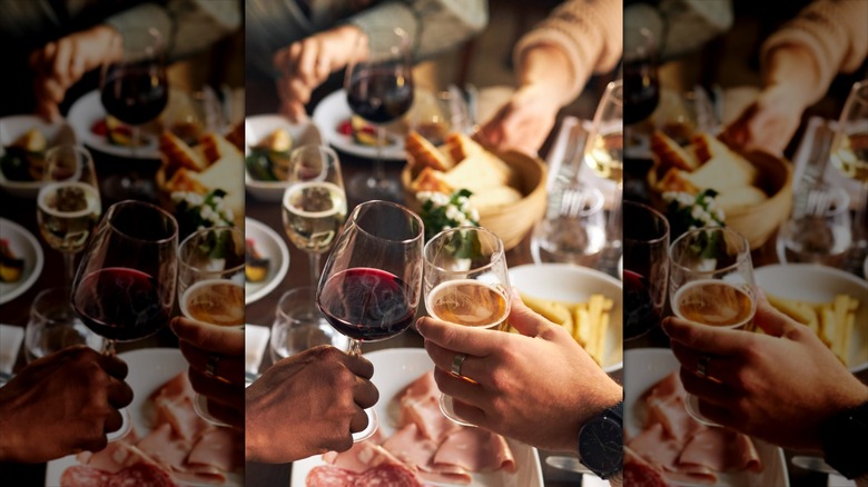 Hands toasting with wine glasses, with a full dinner table in background