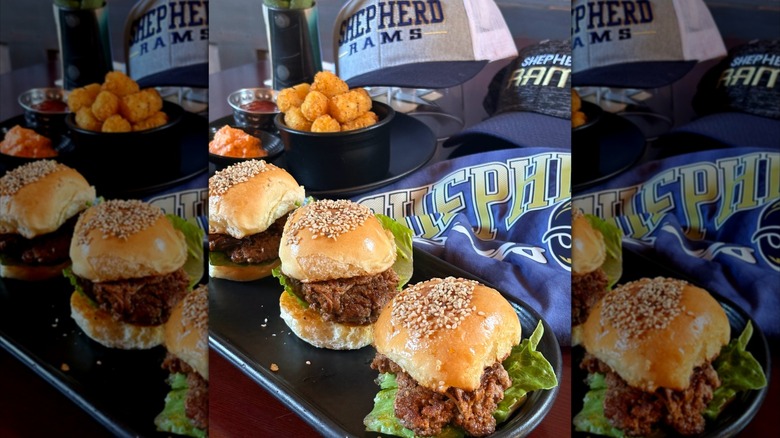 A tray of burgers and tots with a Sheperdstown University hat and shirt