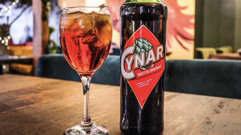 A glass of Cynar Spritz in a tall glass with original Cynar bottle next to it