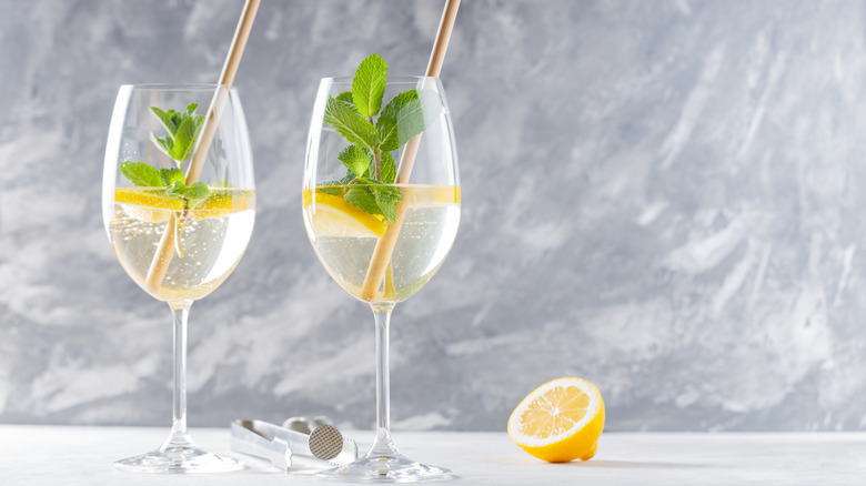 Two glasses of Hugo Spritz with lemon and tongs against a blue background