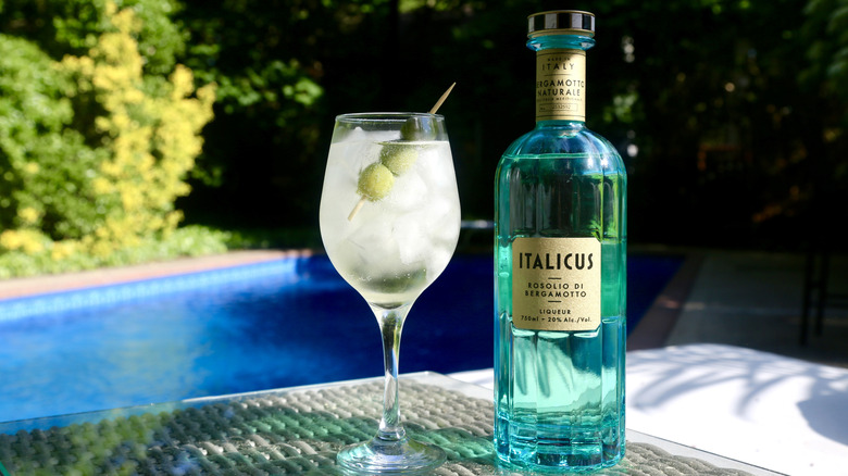 A glass of Italicus Spritz with olive garnish and Italicus bottle next to it and a pool in the back