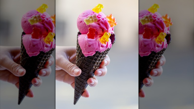 A dark ice cream cone with pink scoop of ice cream topped with gummy bears