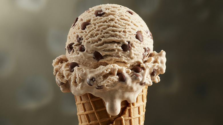 A scoop of drippy ice cream on a cone, topped with chocolate chips
