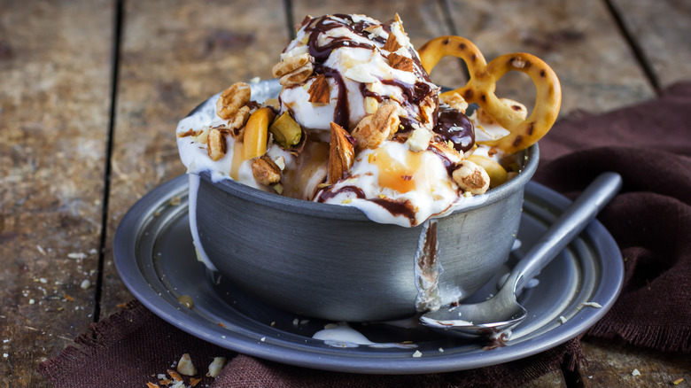 Melty ice cream in a bowl with nuts and pretzels as toppings