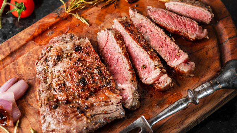 Cooked sliced steak on wooden cutting board